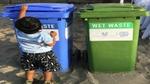 An image of a young boy throwing garbage into a dry waste trash can which is placed next to a wet waste trash can.