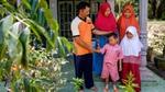 Indonesian oil palm smallholder famer and his family, including two young children, standing on the porch of their house