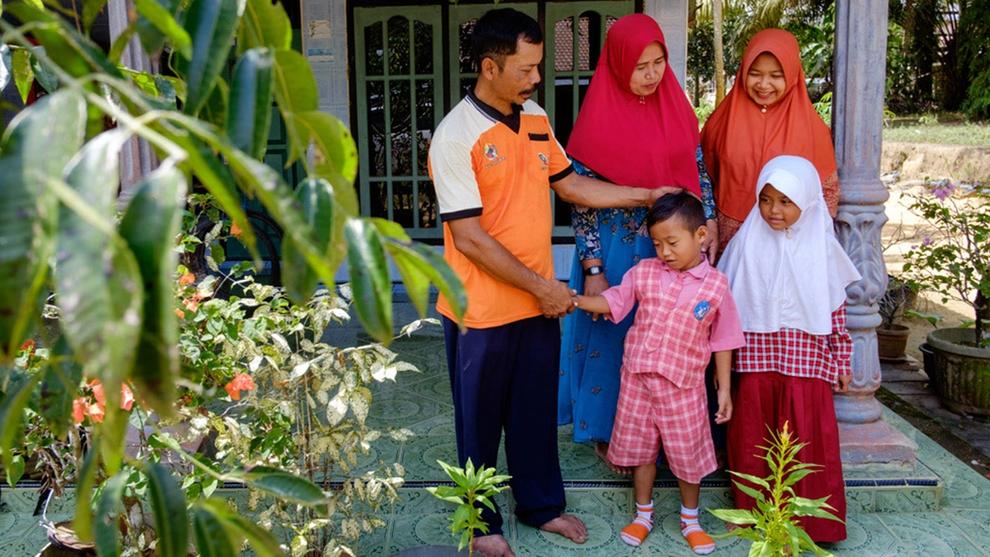 Indonesian oil palm smallholder famer and his family, including two young children, standing on the porch of their house
