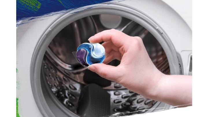 A person placing an OMO capsule into their washing machine.