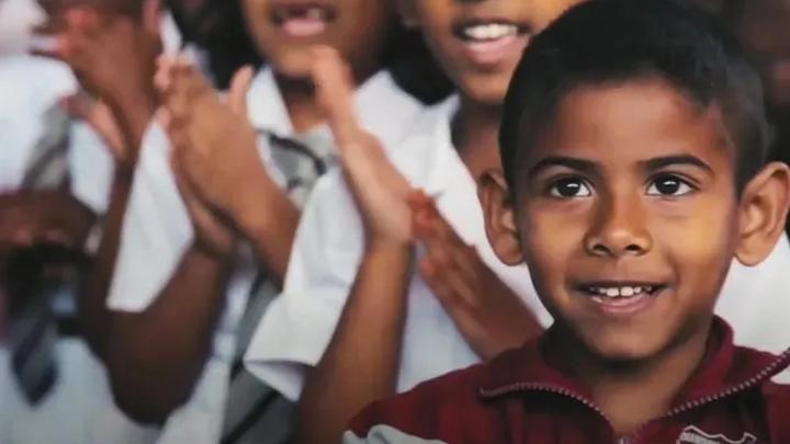 A boy smiling with people behind him rubbing their hands