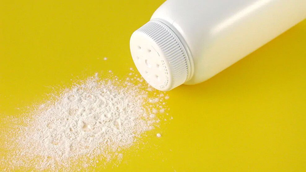 Bottle of talcum powder with some powder on yellow surface