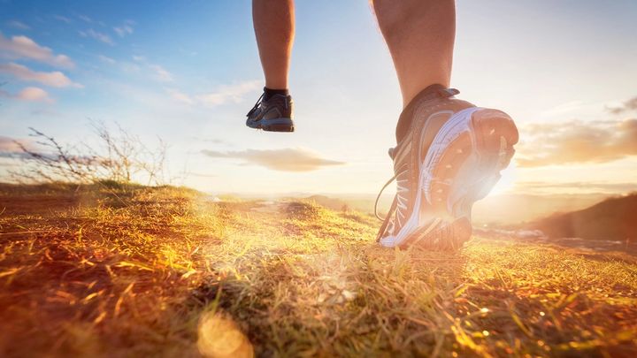 Bare legs wearing trainers running over a baron field at sunset