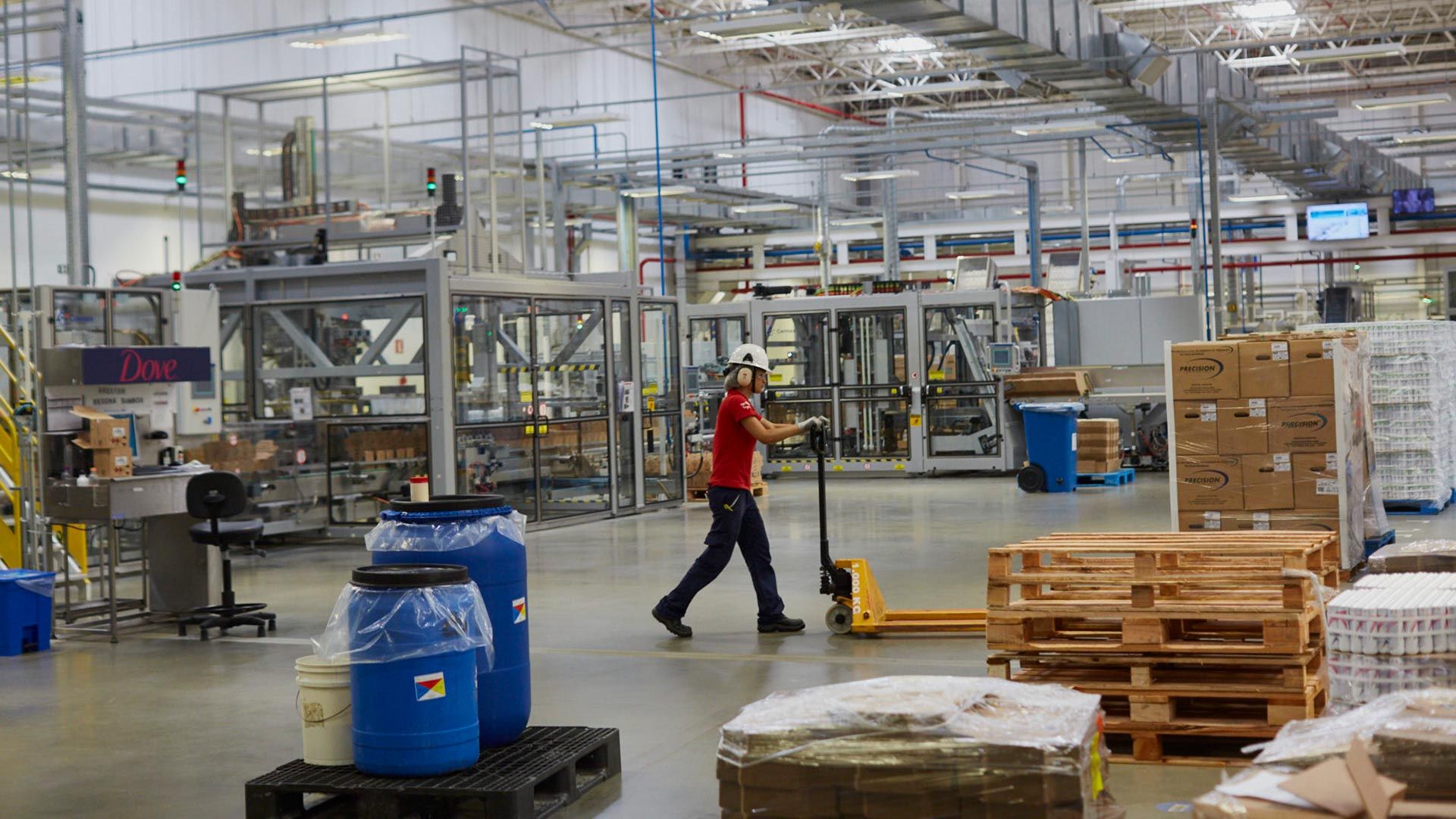A person wearing a hardhat pushes a trolley across a factory floor
