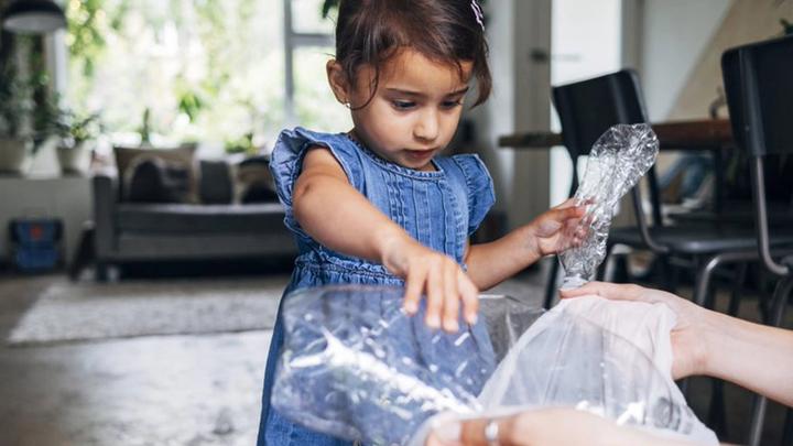 Little girl and adult helper sorting plastic food packaging for recycling