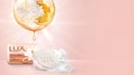 A bar of Lux soap and an orange bubble containing a slice of orange and some white flowers. All on a pink background.