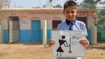 A young schoolboy outside a toilet in India holds up a poster about keeping toilets clean