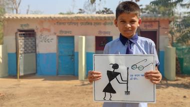A young schoolboy outside a toilet in India holds up a poster about keeping toilets clean