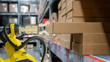 A robotic arm selects a cardboard package from a stack in a warehouse