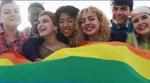 Young diverse people having fun holding LGBT rainbow flag outside