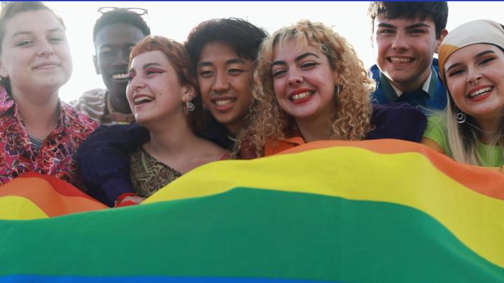 Young diverse people having fun holding LGBT rainbow flag outside