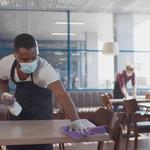 Two people wearing facemasks wiping down tables in a restaurant