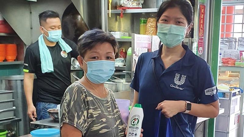 Three people wearing masks in a commercial kitchen with Unilever employee giving a bottle of Cif to the owner.