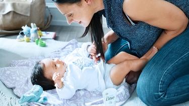 A baby is on the table with her mom holding her. She is wrapped in a towel after being bathed with Dove gentle baby products.
