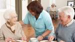 Two seniors being served a sandwich by a care assistant