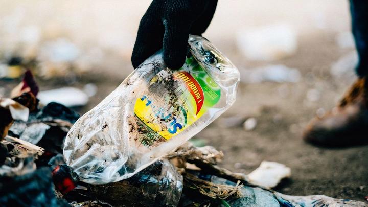 Gloved hand picking up discarded Sunlight plastic bottle from the ground for it to be collected and recycled.