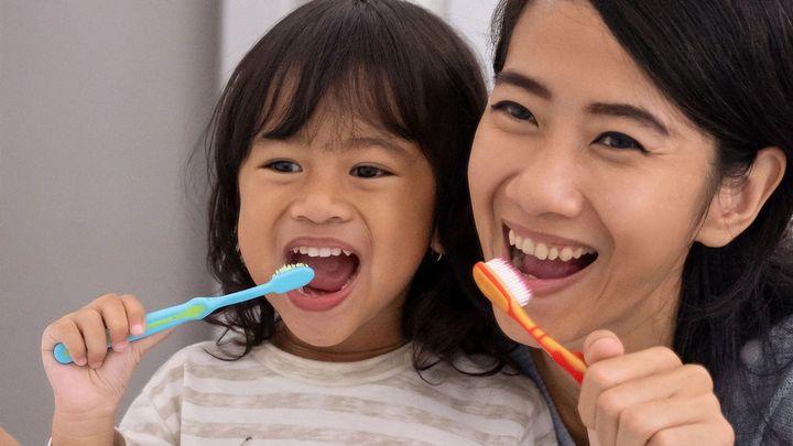 Mother and toddler daughter cleaning their teeth side by side at the bathroom sink