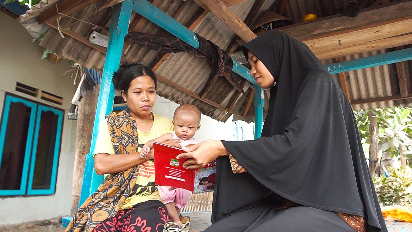 Mother holding a baby being shown a brochure by another woman