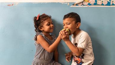 Two children share a bite of apple