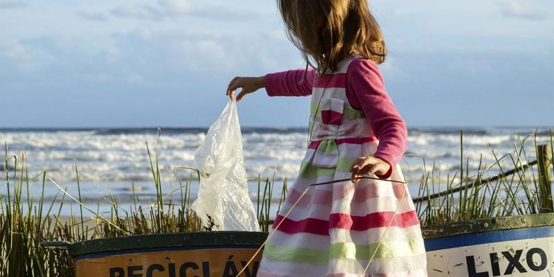 girl on a beach recycling a plastic bag