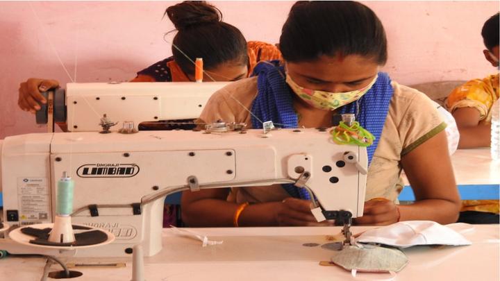 An image of female workers sitting next to a sewing machine, making masks.  