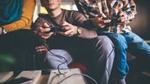 Photo focused in on the hands of three people sitting on a sofa using games consoles to play an online game