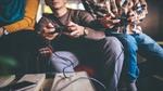 Photo focused in on the hands of three people sitting on a sofa using games consoles to play an online game