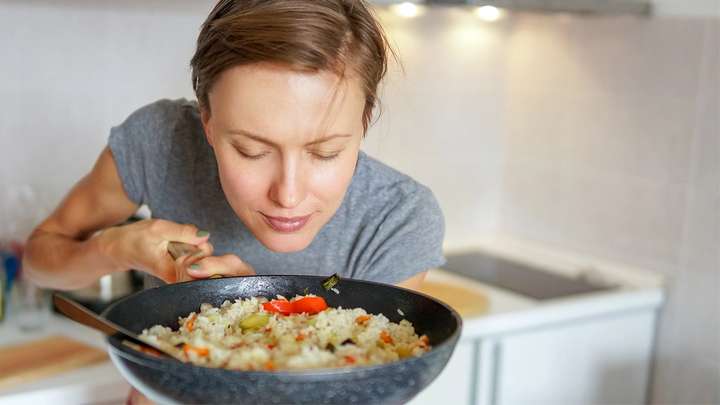 A woman savouring the aroma of a pan of rice and vegetables