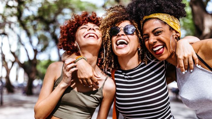 3 smiling women with their arms around each other's shoulders, before social distancing guidelines were introduced.