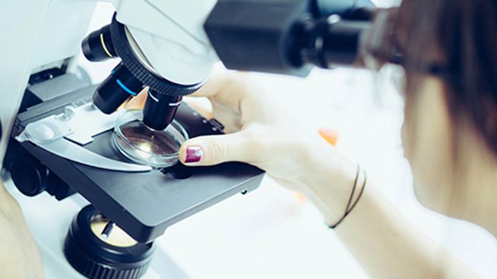 close up of a lady looking through a microscope at a sample in a petri dish