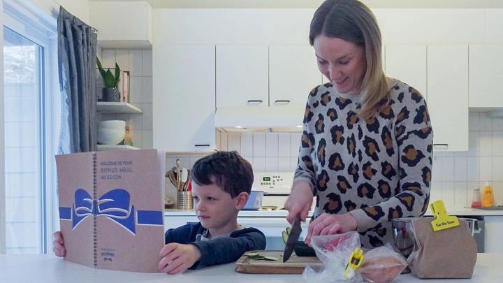 Mother and child in kitchen preparing a meal from a Hellmann’s recipe book.
