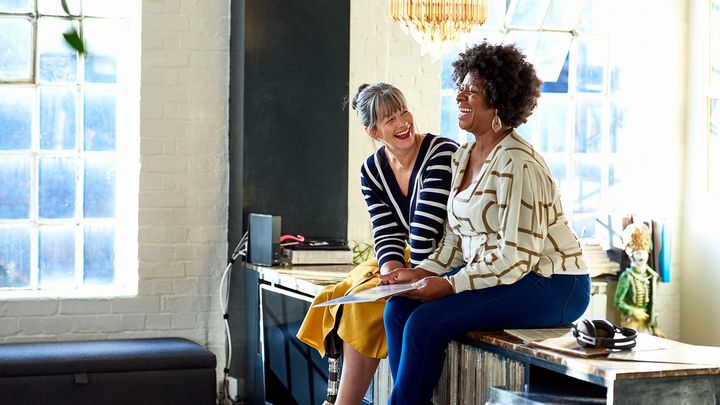Two women sitting talking on a desk in an office