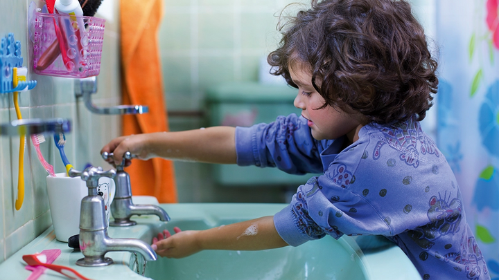Young boy with curly hair runs water from a bathroom sink