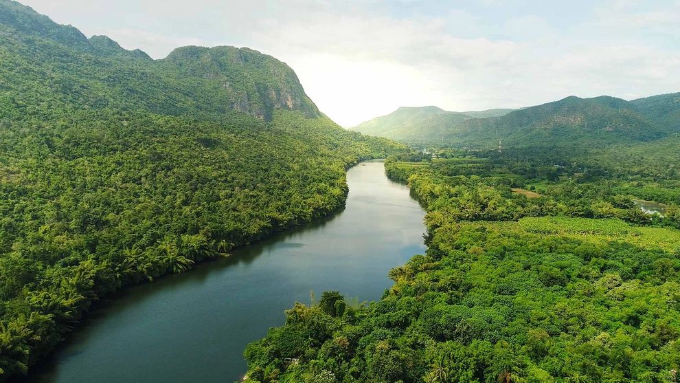 Aerial view of river in tropical green forest with mountains in background