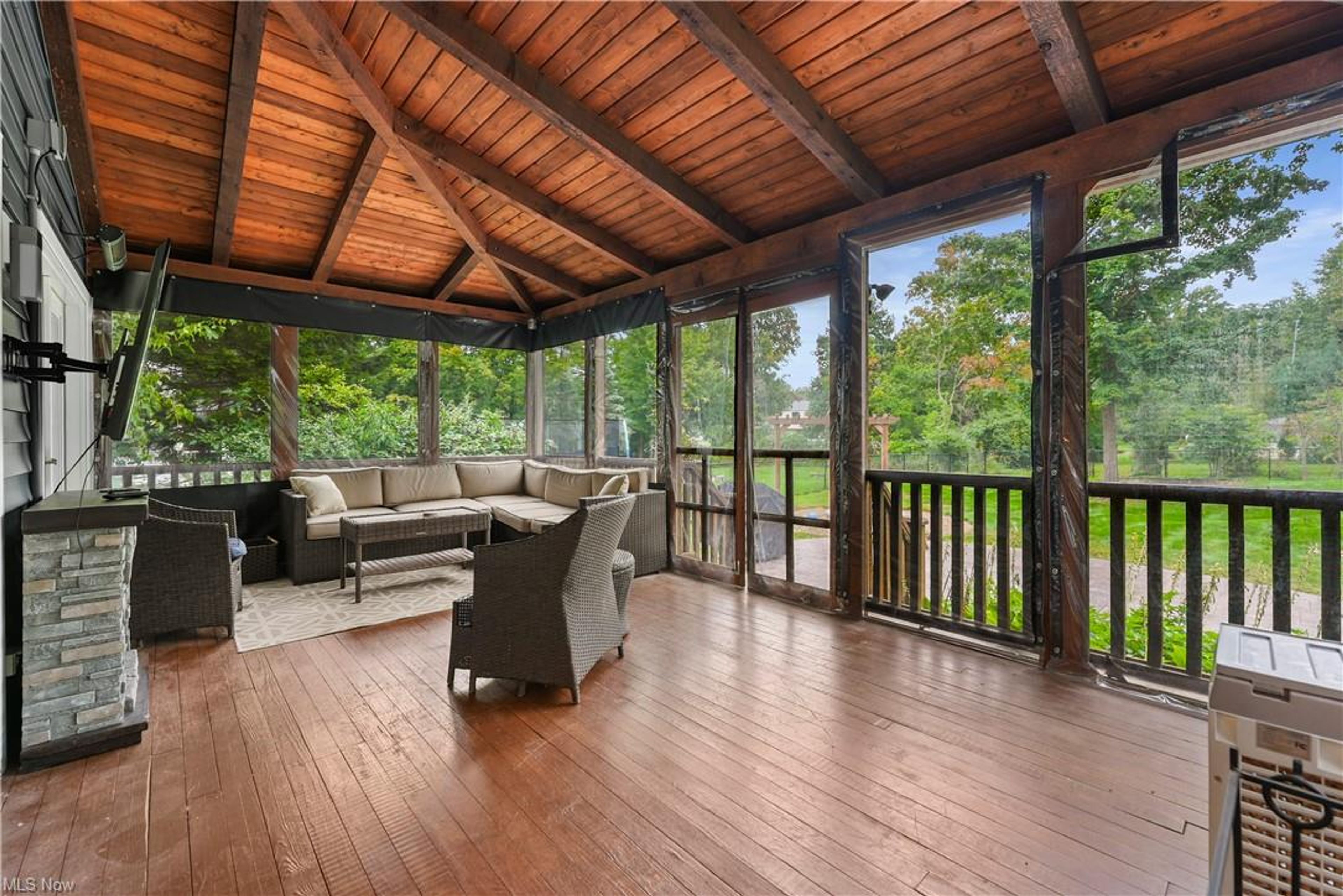 Screened porch with vaulted wood ceiling, mounted TV, and backyard views