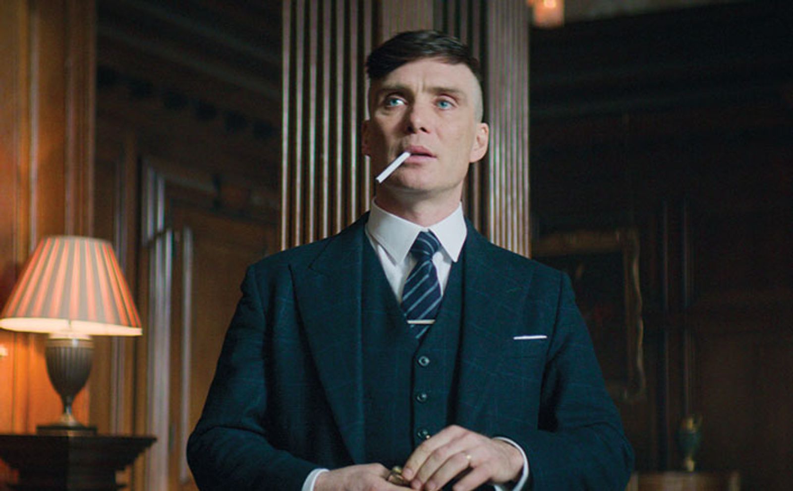 Thomas Shelby in Peaky Blinders smoking a cigarette and dressed in a suit.