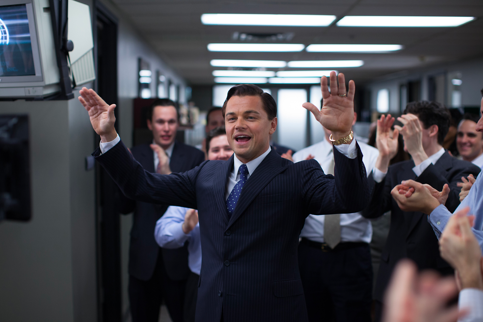 Leonardo DiCaprio as the charismatic Wolf of Wall Street Jordan Belfort  dressed in a suit and raising his hands to his many employees.