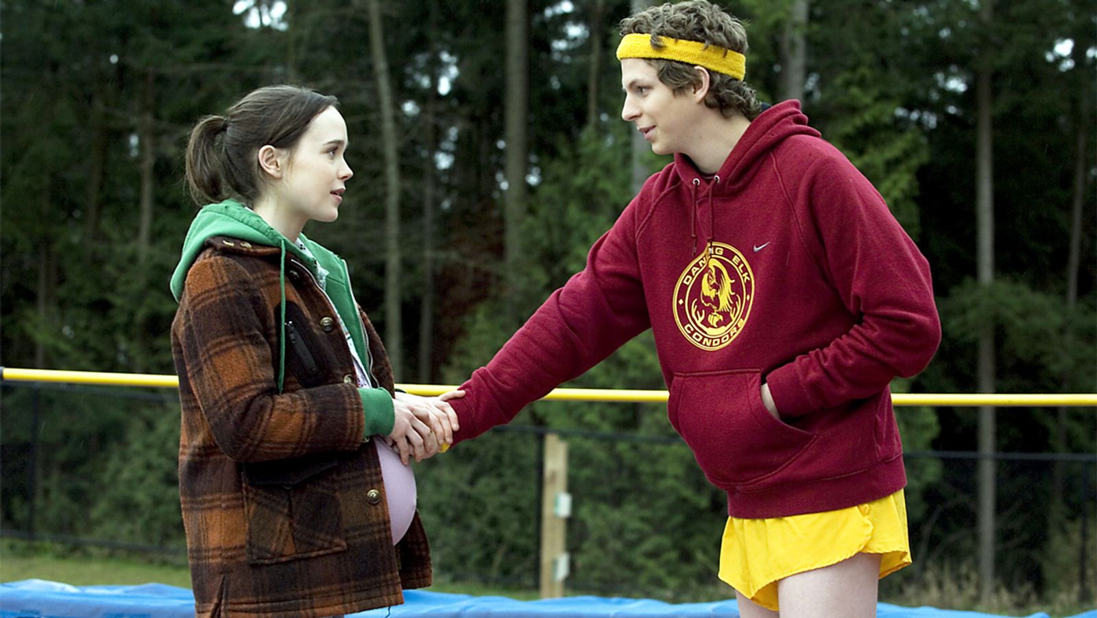 A pregnant Juno shaking hands whilst Paulie at a camp in the middle of the woods