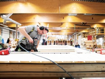 a man is cutting a piece of wood with a circular saw in a factory .