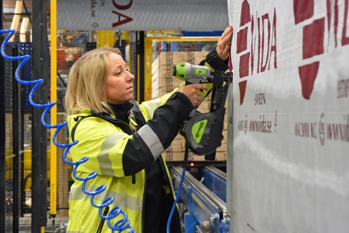 a woman in a yellow jacket is working in a sawmill to wrap lumber .