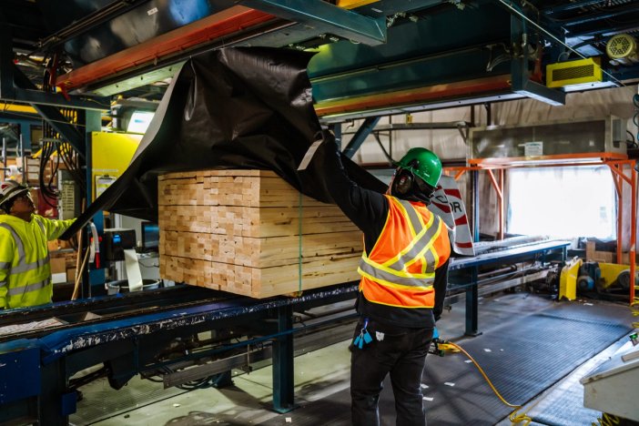 a man applies wrapping to a stack of lumber in a factory .