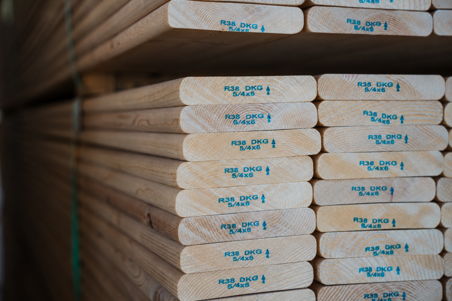 Stack of lumber boards with blue stamps "R38 DKG 5/4x6" on their ends.