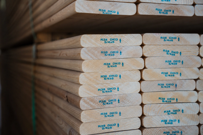 Stack of lumber boards with blue stamps "R38 DKG 5/4x6" on their ends.