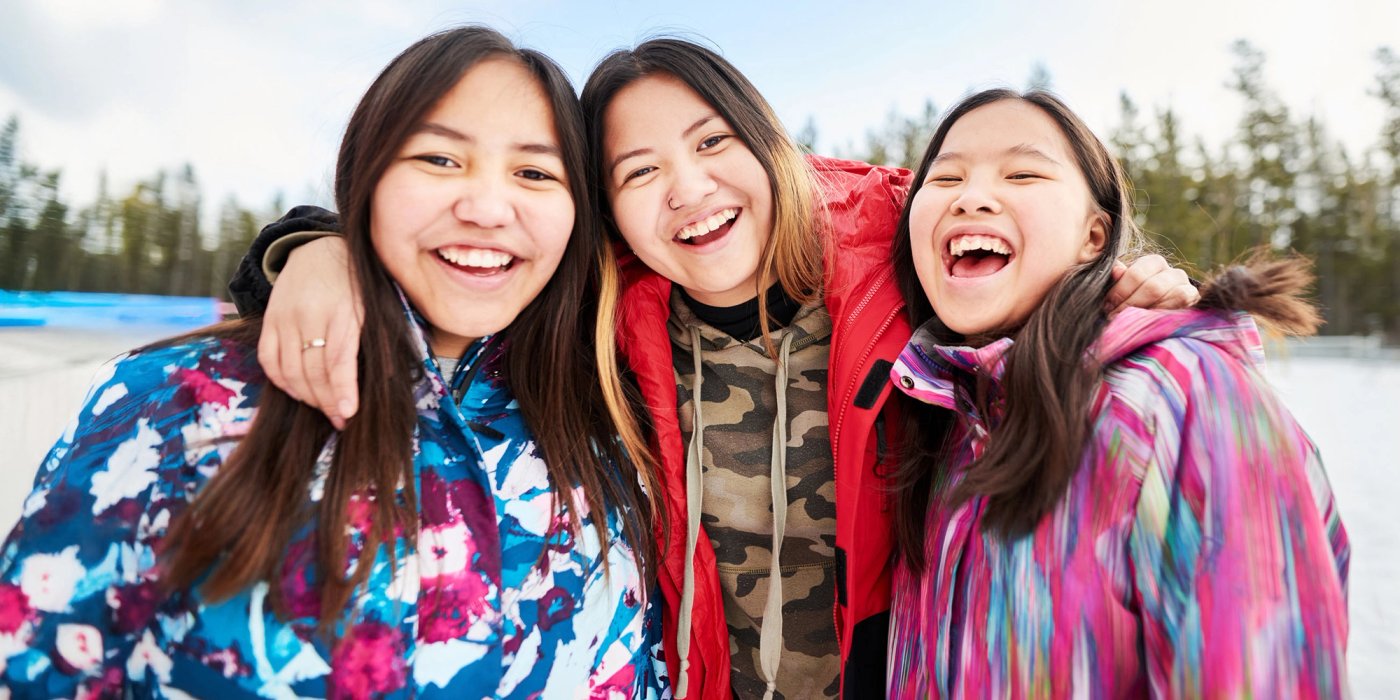 three young Indigenous women are smiling and laughing, posing for a picture in the snow .