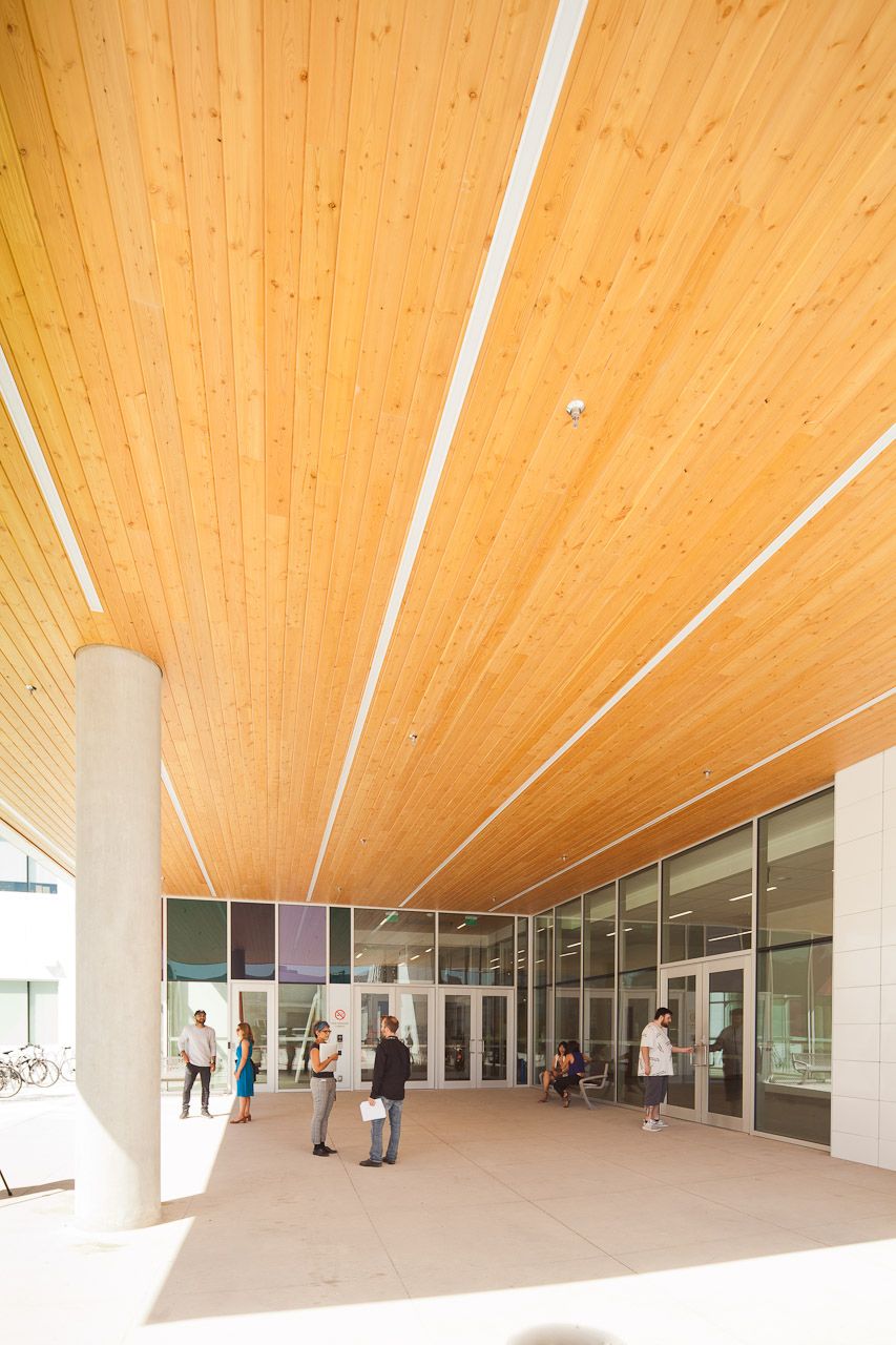 a group of people standing outside of a building with a wooden ceiling