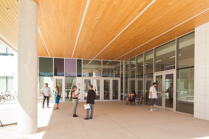 a group of people standing outside of a building with a wooden ceiling