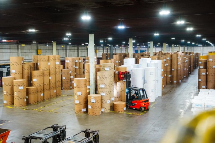 a large warehouse filled with lots of rolls of paper and a forklift .