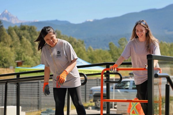 two women are smiling and laughing while pushing a utility cart at a volunteer event. .