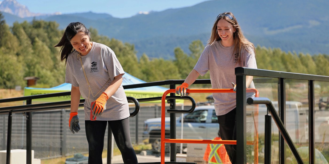 two women are smiling and laughing while pushing a utility cart at a volunteer event. .