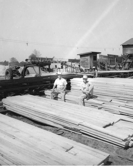 Old photo of two people sitting on lumber